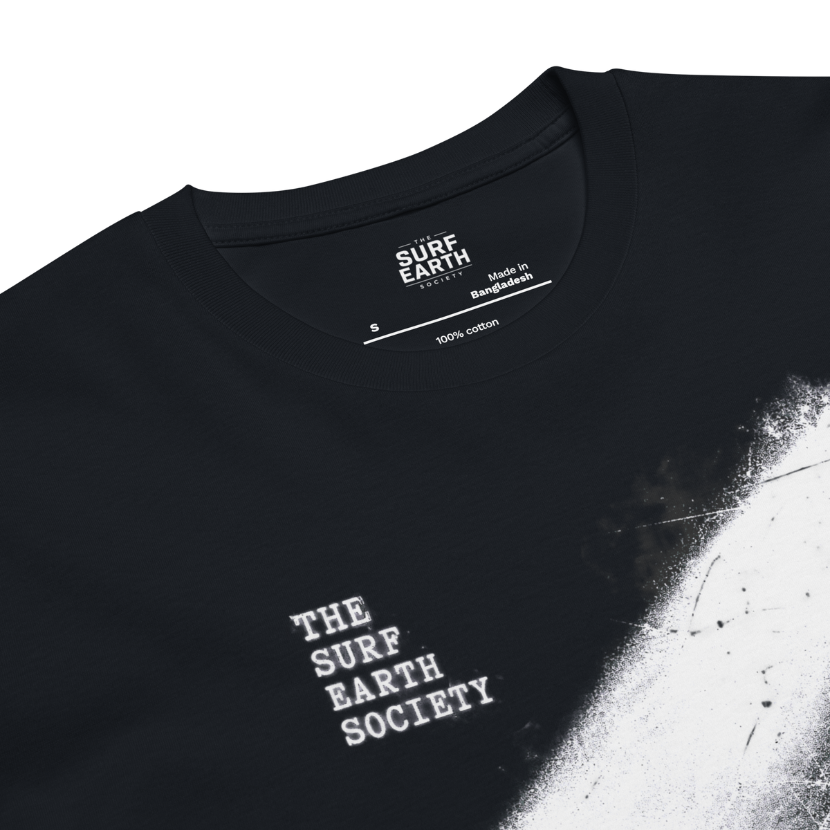 Close-up of a navy t-shirt showing the inner neck label with 'SURF EARTH SOCIETY' and '100% cotton', along with 'Made in Bangladesh' and 'S' size. The front has a white distressed paint-splatter graphic on the right side and stacked white text reading 'THE SURF EARTH SOCIETY' on the left chest.