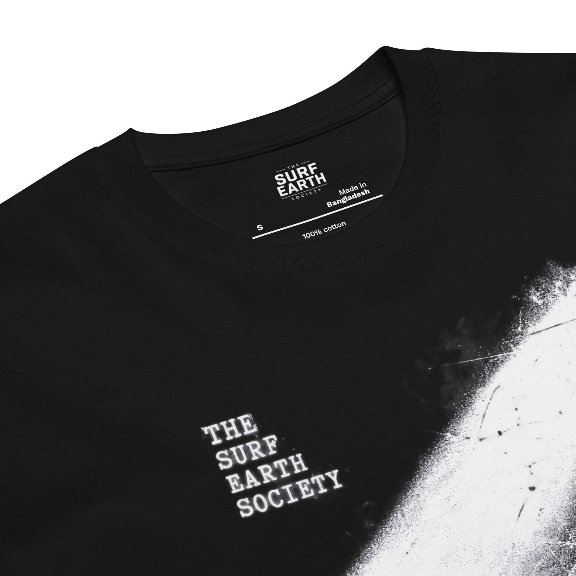 Close-up of a black t-shirt showing the inner neck label with 'SURF EARTH SOCIETY' and '100% cotton', plus white distressed text on the chest and a white paint-splatter graphic on the right side.