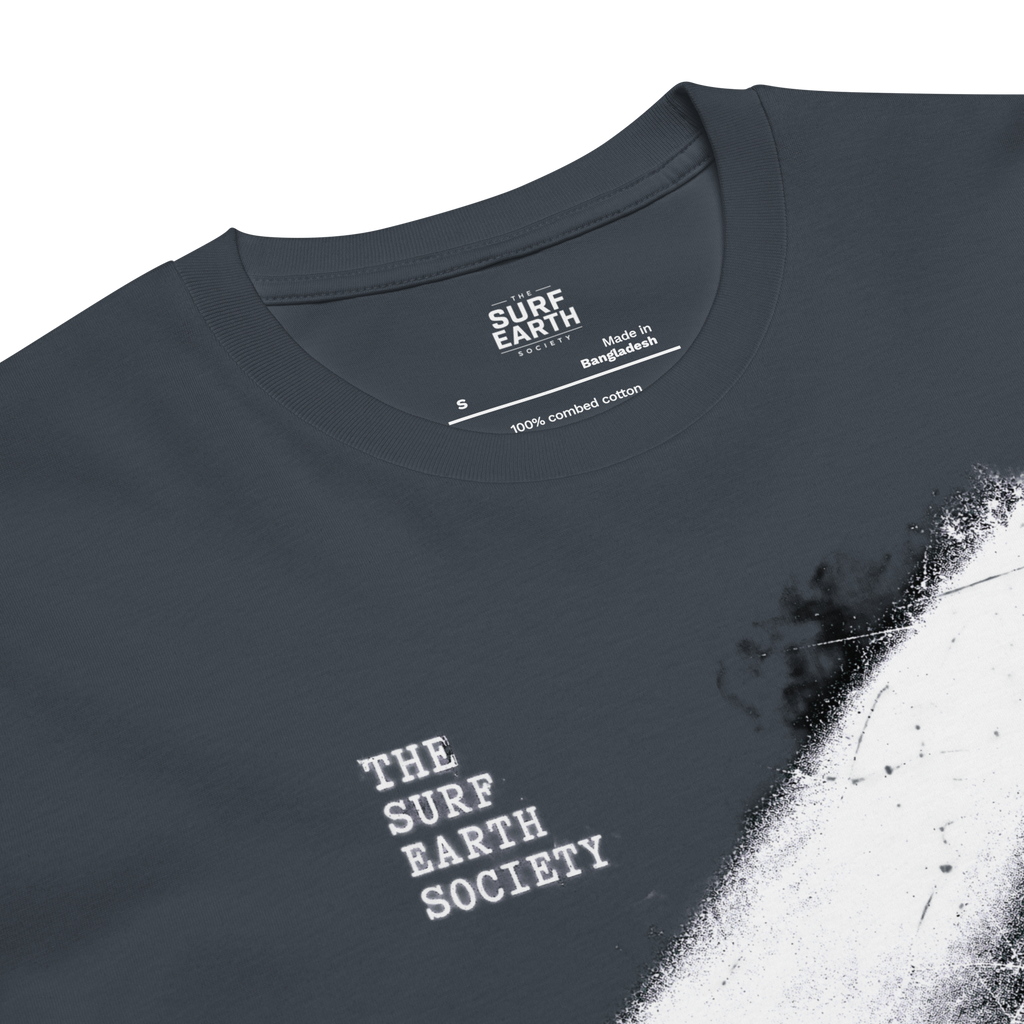 Close-up of a petrol blue gray t-shirt with a white distressed paint-splatter graphic on the right side and 'THE SURF EARTH SOCIETY' printed in white on the chest. The inner collar label shows 'SURF EARTH SOCIETY' and 'Made in Bangladesh'.